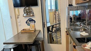 Una cocina con una mesa de madera, taburetes de bar, un reloj y un televisor montado en la pared.