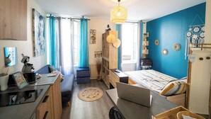 Habitación compacta con cama, escritorio y computadora portátil, que destaca por una pared azul y una lámpara colgante.
