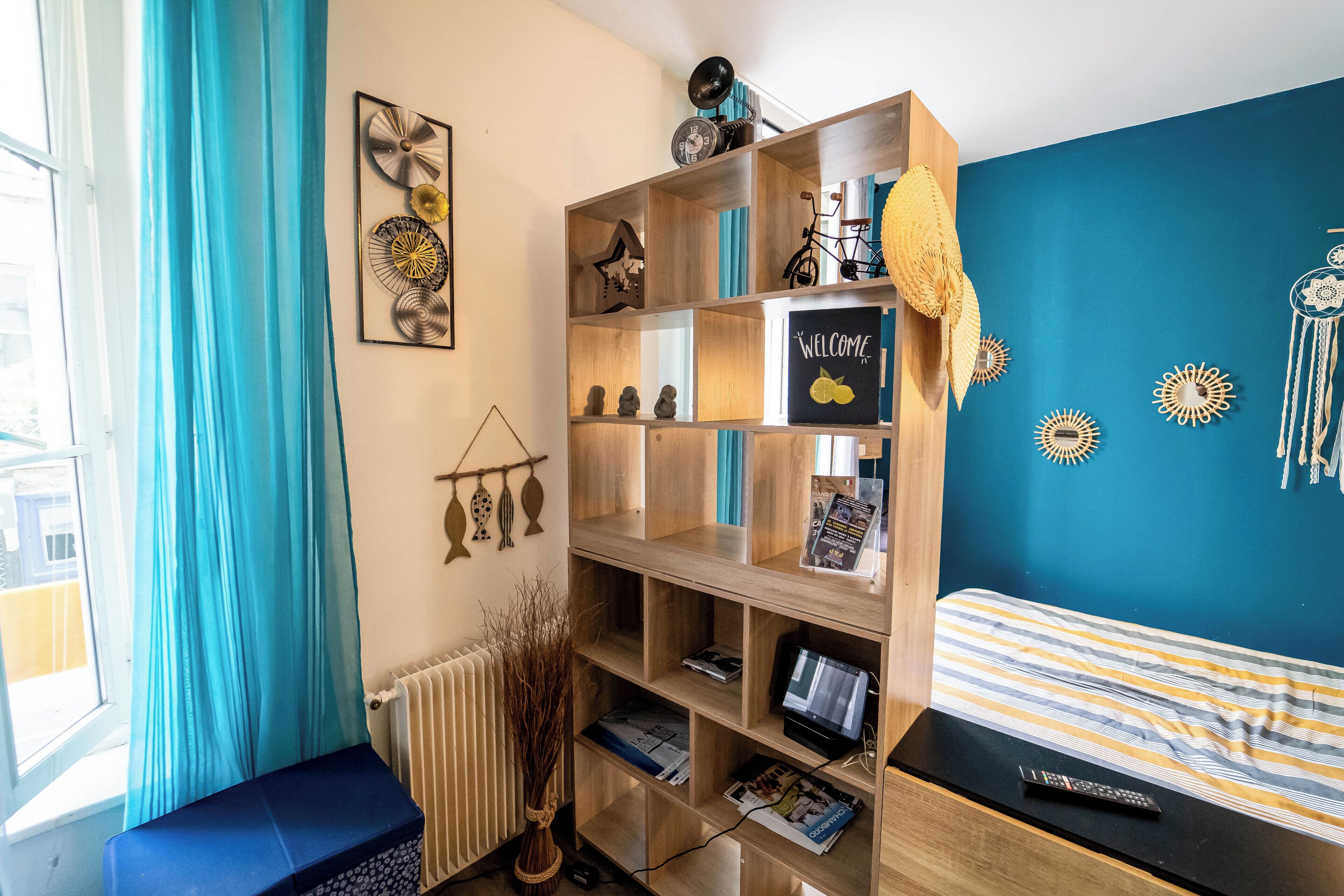 A room with a bed, a wooden bookshelf, a radiator, and a window with curtains.