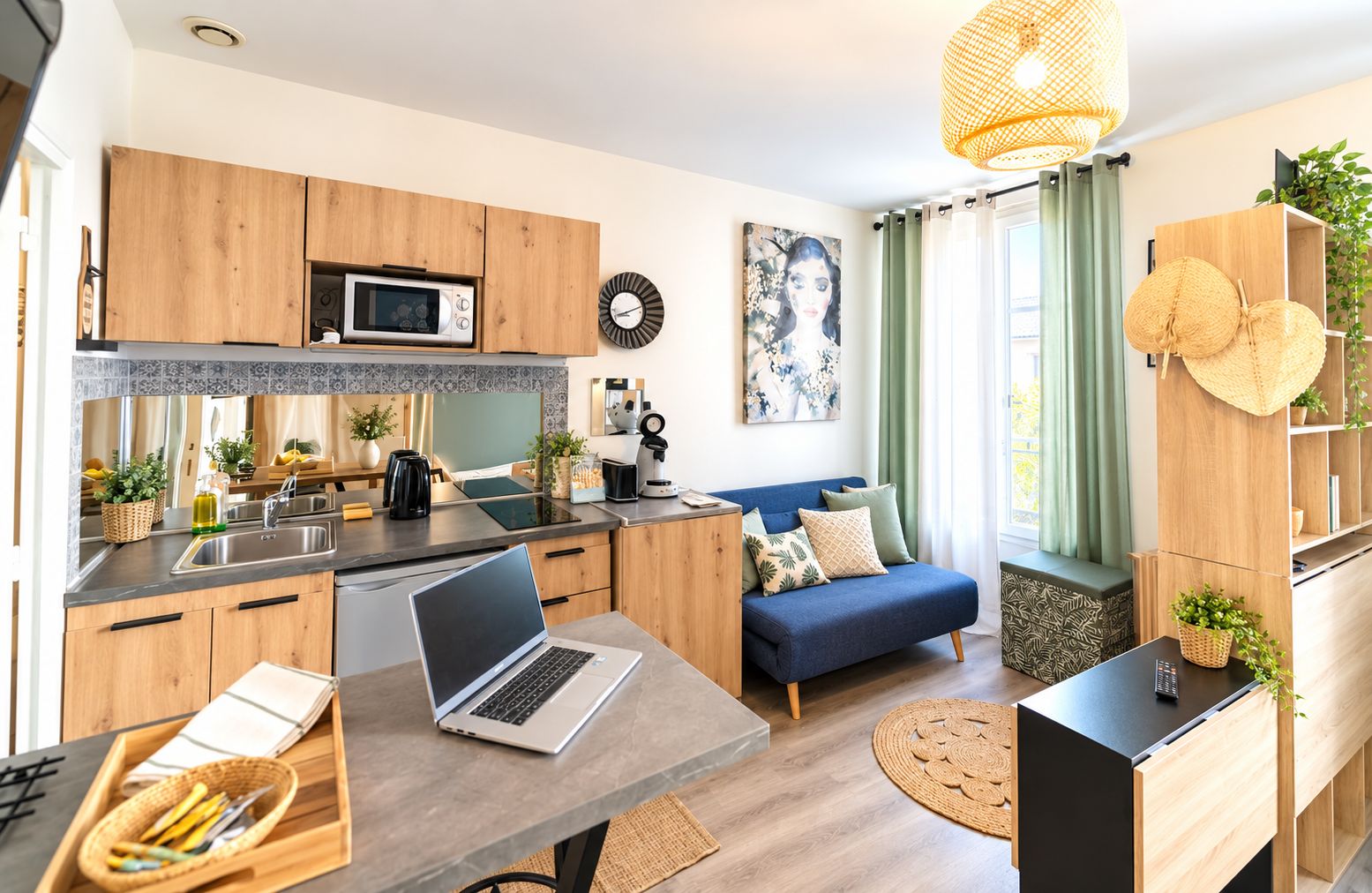 A modern kitchen with wooden cabinets, a microwave, and a coffee maker. There's a blue sofa with cushions, a laptop on a table, and a large window with curtains.