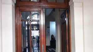 Ein rundbogiger Durchgang mit hölzernem Rahmen und Glasscheiben, der in einen Korridor mit Fliesenboden und Marmorverkleidung führt.