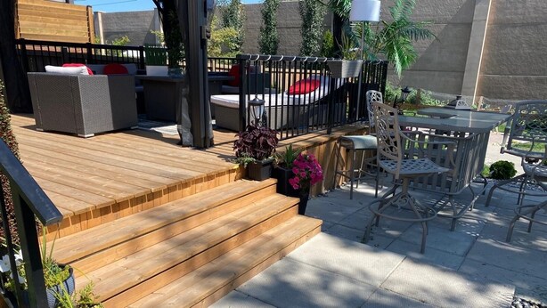 Eine Holzterrasse mit Gartenmöbeln, darunter eine Couch und Stühle sowie ein Tisch.