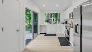 Eine moderne Küche mit weißen Schränken, einem Edelstahlkühlschrank und Blick auf einen Wald durch ein großes Fenster.