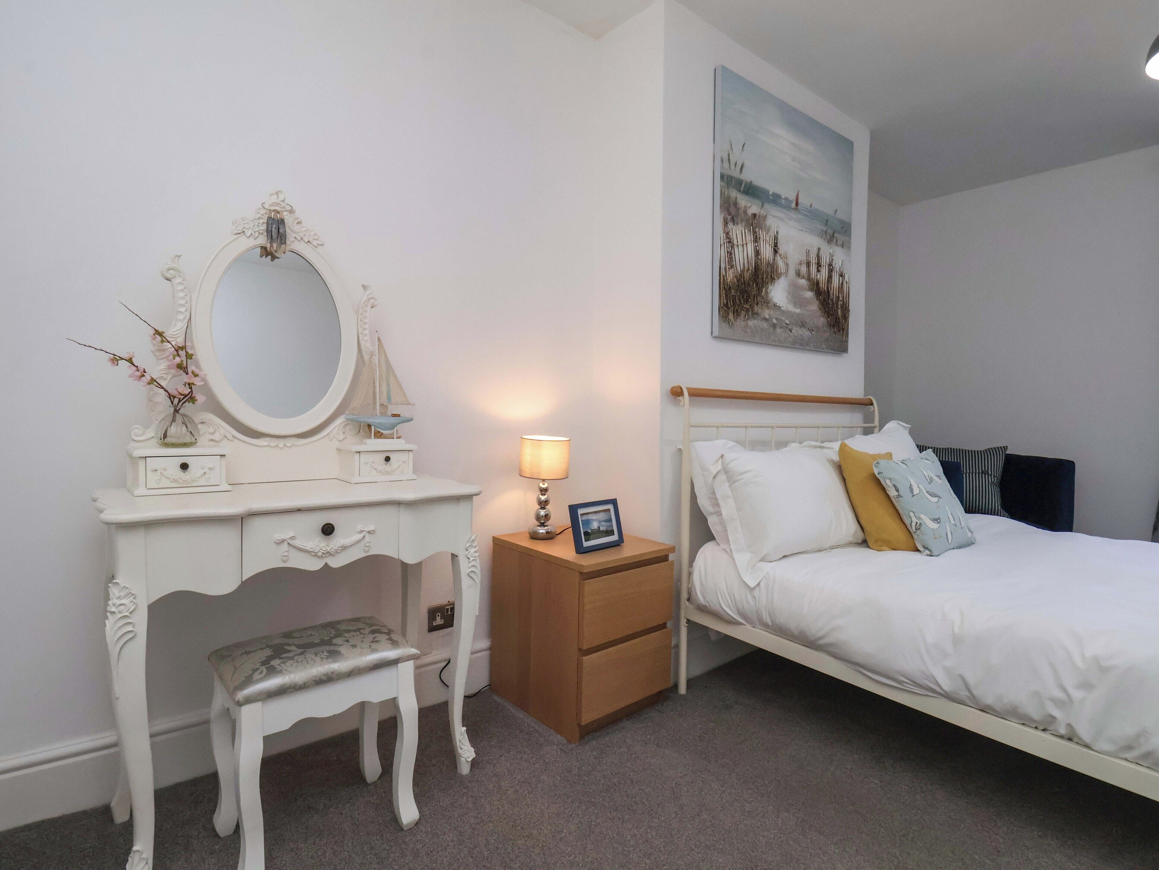 A bedroom with a bed, a nightstand, a dresser with a mirror, a chair, and a painting on the wall.