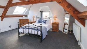 Ein Schlafzimmer im Dachgeschoss mit schrägen Wänden, einem Bett mit Metallgestell, zwei Nachttischen mit Lampen, einer Holzkommode und einem Dachfenster.