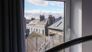 Ein Fenster mit Blick auf eine Stadtansicht, darunter Gebäude mit zahlreichen Schornsteinen und einem klaren Himmel.