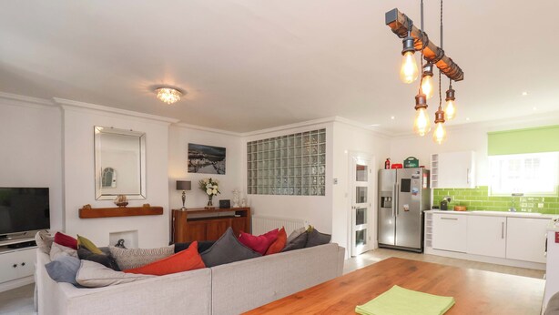 Ein modernes Wohnzimmer mit Sofa, Couchtisch und Küchenzeile mit Kühlschrank und grüner Spritzschutz.