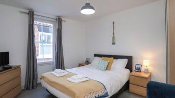 A bedroom with a bed, bedside tables, a desk, a chair, a window with curtains, and a hanging lamp.