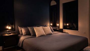 Un dormitorio con una cama grande, dos mesitas de noche con lámparas, un espejo amplio y una ventana.