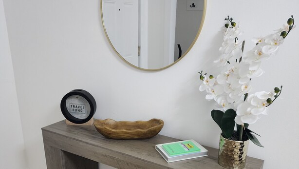 A wooden console table with a round mirror, a small clock, a decorative plant, and a woven basket. - 3-bedroom two story house in tranquil Metropolis with cool AC breeze (Metropolis)