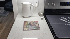 A kitchen with white cabinets, a white countertop, a kettle, a digital clock, and a stove. - 3-bedroom two story house in tranquil Metropolis with cool AC breeze (Metropolis)