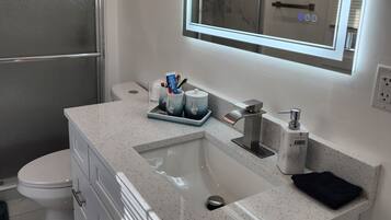 A modern bathroom with a white marble sink, a large mirror with LED lighting, and a toilet.