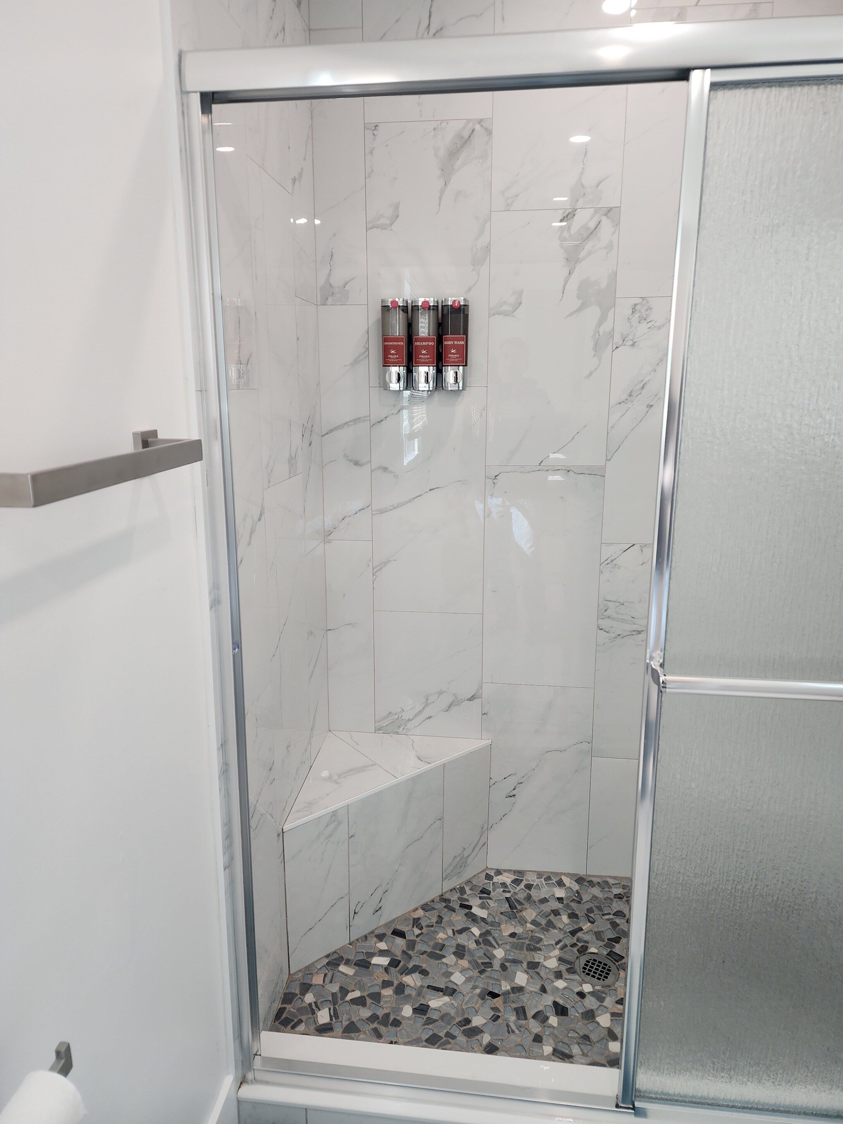 A glass-enclosed shower with a marble wall and a mosaic floor.