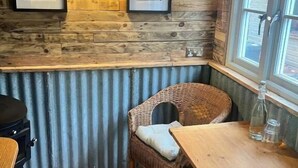 Ein Eckzimmer mit Holzwänden, einem Korbstuhl, einem Holztisch und gerahmten Bildern an der Wand.