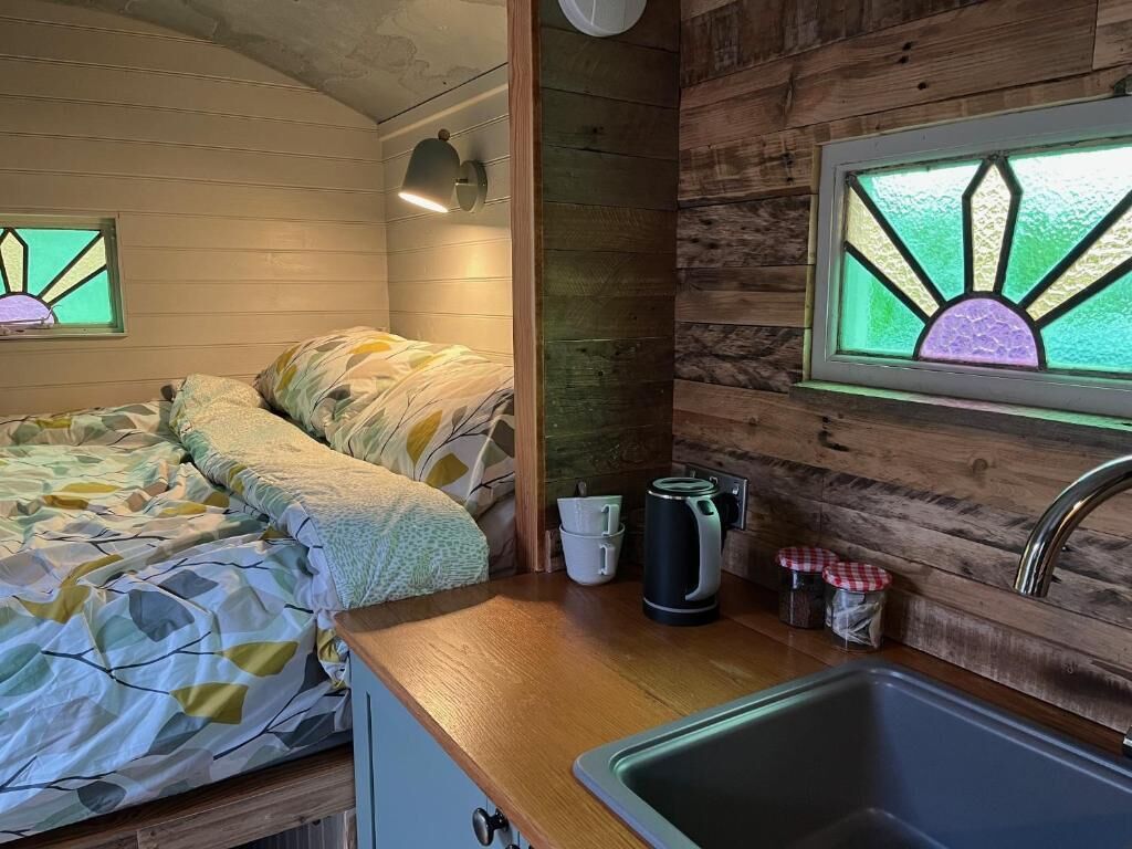 Interior acogedor de una cabaña con cama, kitchenette y una ventana con diseño de vitral.