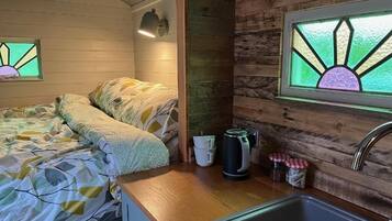 Interior acogedor de una cabaña con cama, kitchenette y una ventana con diseño de vitral.