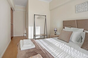 A bedroom with a bed, a bedside table, a hanging clothes rack, and a door. - Apartment 'Sérénité' with Balcony, Wi-Fi and Air Conditioning (Ponta Delgada)