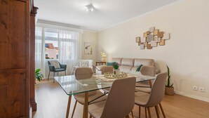A modern living room with a glass dining table, beige sofa, and a decorative wall piece. - Apartment 'Sérénité' with Balcony, Wi-Fi and Air Conditioning (Ponta Delgada)