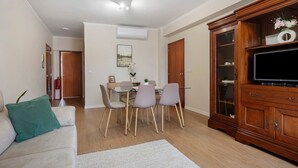 A living room with a sofa, a dining table with chairs, a TV cabinet, and a painting on the wall. - Apartment 'Sérénité' with Balcony, Wi-Fi and Air Conditioning (Ponta Delgada)