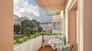 A balcony with a table and chairs, a potted plant, and a view of the street and buildings. - Apartment 'Sérénité' with Balcony, Wi-Fi and Air Conditioning (Ponta Delgada)