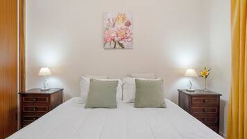 A neatly made bed with white bedding, two bedside tables with lamps, and a floral artwork on the wall.