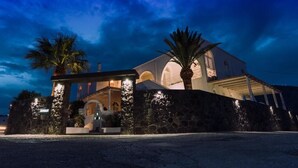 A large, two-story building with a stone facade, arched windows, and a well-lit entrance. - Blue Life hotel (Santorini)