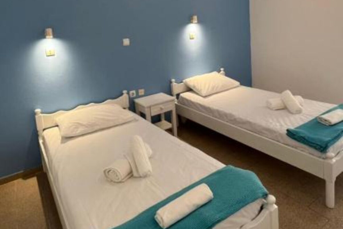 A hotel room with two single beds, a small bedside table, a wall-mounted light fixture, and a ceiling light.