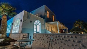 A building with a stone facade, arched windows, and a covered outdoor seating area. - Blue Life hotel (Santorini)