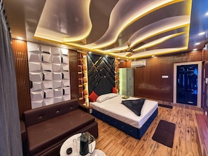 A modern hotel room with a bed, a sofa, a small table, and a ceiling with unique lighting. - Hotel aj plaza (Mayapur)