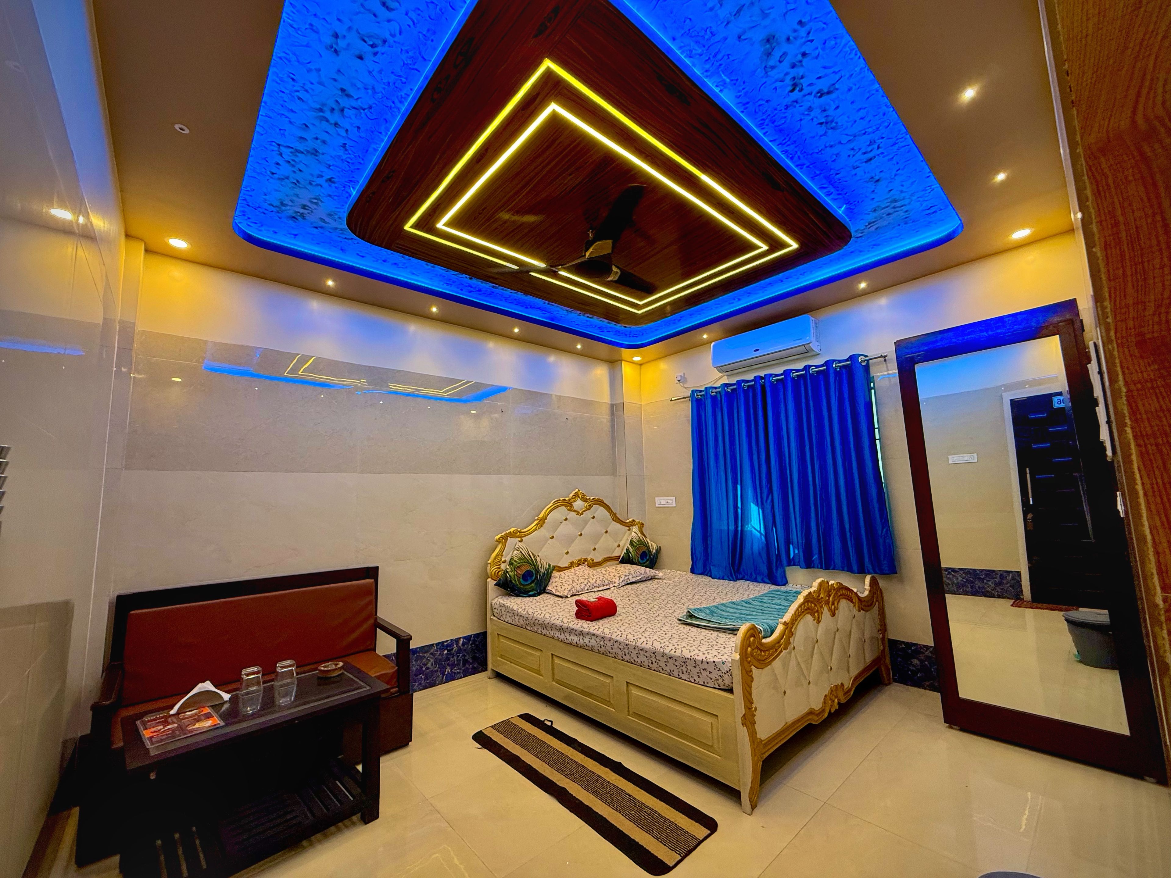 A bedroom with a bed, a vanity, a mirror, and a ceiling with blue lighting.
