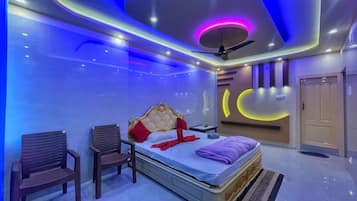 A modern bedroom with a bed, two chairs, a ceiling fan, and a wall-mounted light fixture.