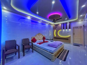 A modern bedroom with a bed, two chairs, a ceiling fan, and a wall-mounted light fixture.