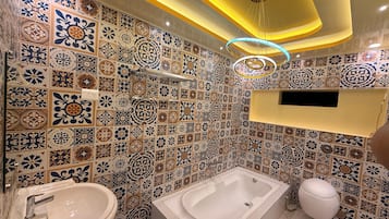 Un baño con bañera, lavamanos e inodoro, que presenta diseños decorativos en azulejos e iluminación empotrada.