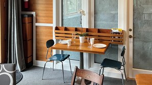Een kamer met houten frame, een eettafel, stoelen, een bankje, een potplant en een brandblusser.