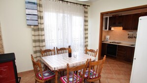 Un coin repas avec une table dressée pour quatre personnes, des chaises en bois avec des coussins colorés, une bouteille d’eau et un calendrier accroché au mur.