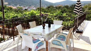 Une terrasse avec une table dressée pour deux personnes, entourée de chaises, un vase rempli de fleurs et un parasol à rayures.