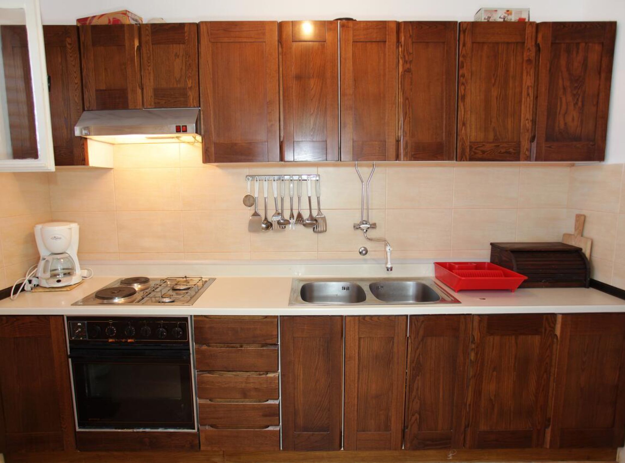 A kitchen with wooden cabinets, a gas stove, a coffee maker, a sink, and a red dish rack.