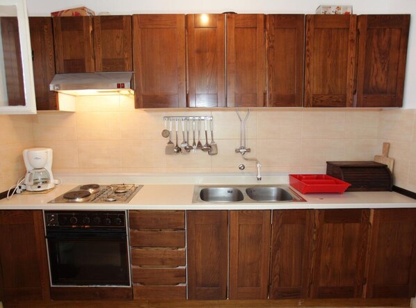 A kitchen with wooden cabinets, a gas stove, a coffee maker, a sink, and a red dish rack. - Apartment Jelena (Marina)