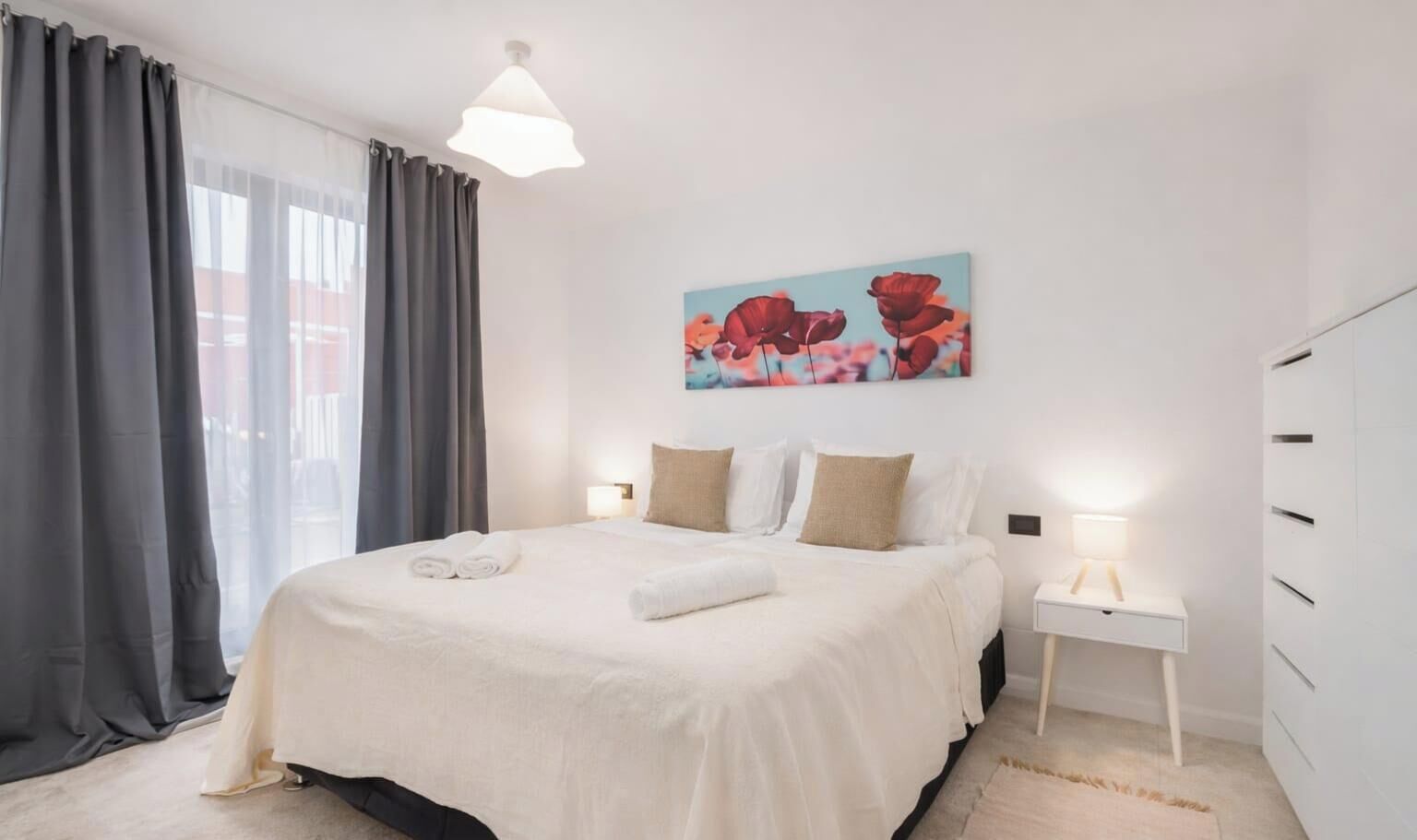 A modern bedroom with a large bed, a bedside table with a lamp, and a painting on the wall.