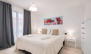 Ein modernes Schlafzimmer mit einem großen Bett, einem Nachttisch mit Lampe und einem Gemälde an der Wand.