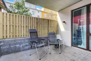 Ein Balkon mit zwei Metallstühlen und einem kleinen Tisch, einem Holzzaun und einer Glastür, die zu einem Gebäude mit gelb-weißen Außenwänden führt.
