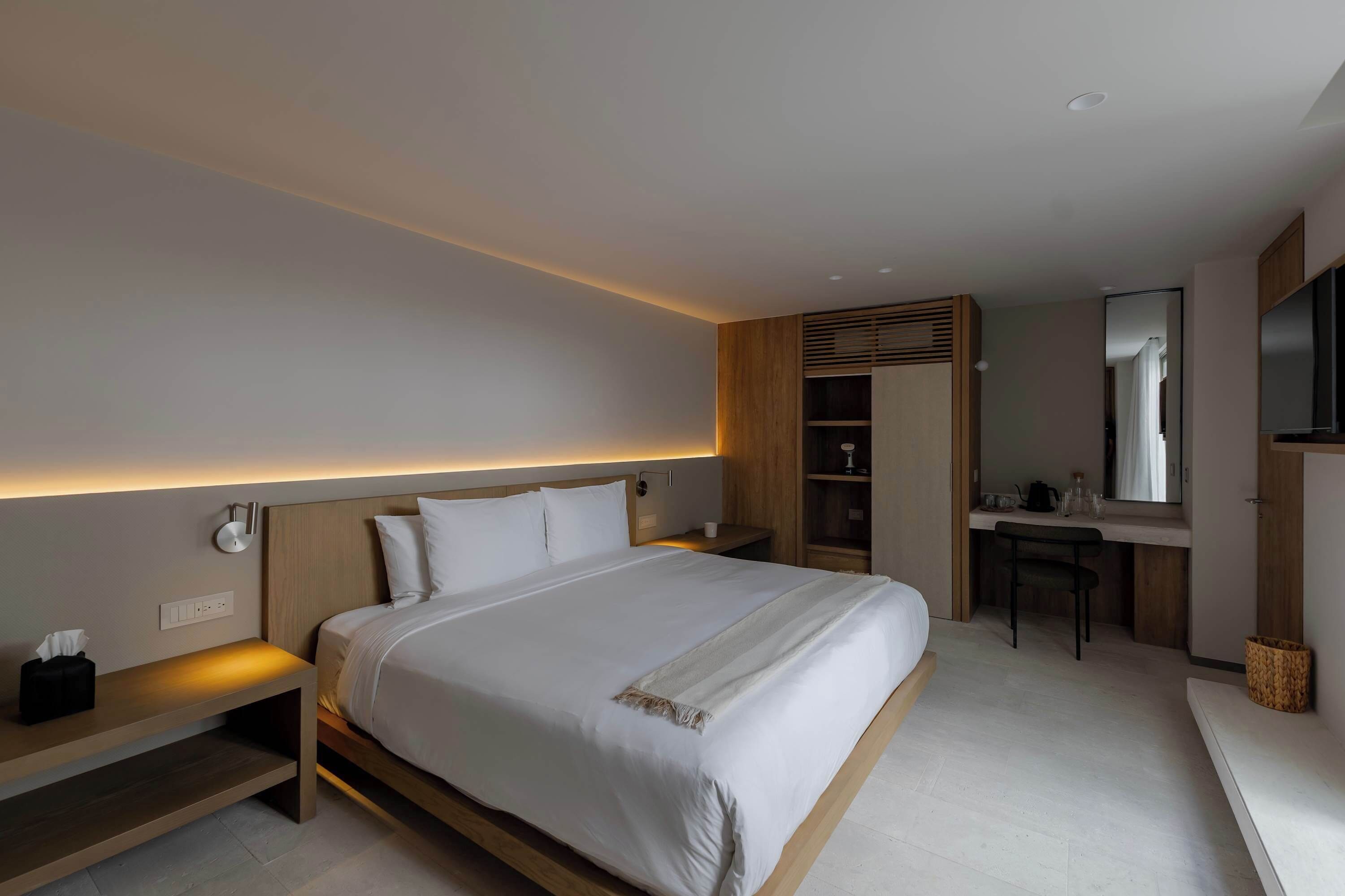 A modern hotel room with a large bed, bedside tables, a desk, and a mirror.