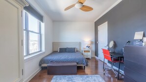 A bedroom with a bed, a desk, a chair, a dresser, and a ceiling fan. - Master King plus 2 Queens by NYC & onsite gym (Jersey City)
