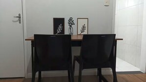 Een kamer met een houten tafel en twee zwarte stoelen. Daarboven hangen kunstwerken in lijsten.