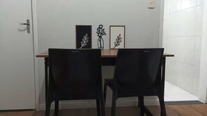 Ein Zimmer mit einem Holztisch und zwei schwarzen Stühlen. Über dem Tisch befinden sich gerahmte Wandbilder.