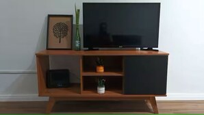 Een houten tv-meubel met een flatscreen televisie, een lijst met foto en twee potplanten.