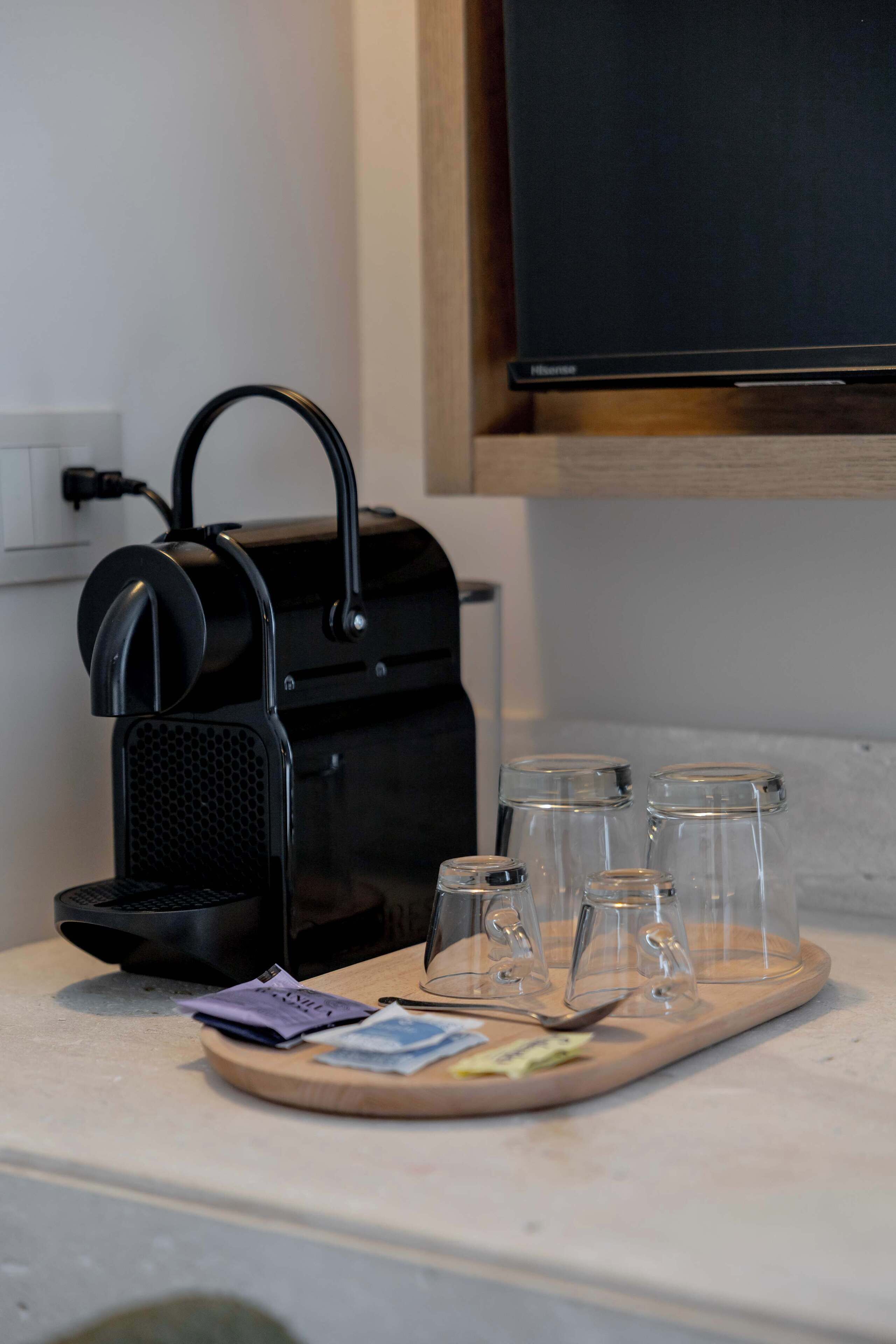 A kitchen counter with a coffee maker, a tray with cups, and a television above.