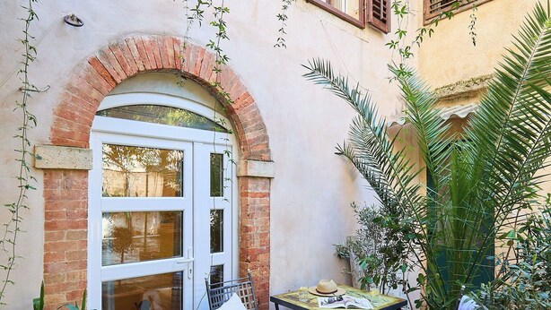 Une cour avec une porte blanche, une petite table entourée de chaises et des plantes en pot.
