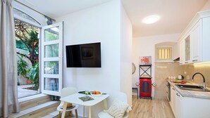 Une cuisine compacte avec un téléviseur, un coin repas avec des chaises, un appareil électroménager rouge et une fenêtre avec des rideaux.