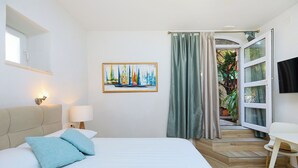 Une chambre à coucher comprenant un lit, une table de chevet, une lampe, un tableau, une fenêtre et une porte donnant sur un balcon.